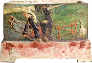 A large ceramic crate that stands on a sturdy base. A scene of a woman on a farm is carved and painted on the front. She is sitting in the grass holding a stick. A black dog and a white duck stand nearby, near a small wooden fence. A large, bright green field of rolling hills is seen in the background.